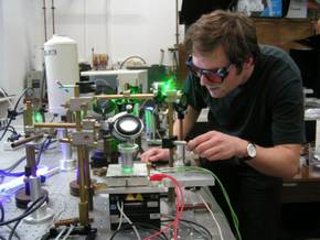 Doktorant Wydziału Fizyki, mgr Kacper Grodecki przygotowuje układ pomiarowy do badań warstw grafenowych. Badana próbka umieszczona jest na stoliku x-y umożliwiającym pozycjonowanie plamki światła laserowego na próbce z dokładnością do ułamków mikrometra. Źródło: Krzysztof Korona, FUW